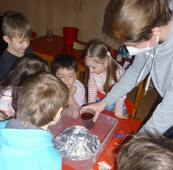 Ein älterer Schüler gießt etwas auf einen Vulkan aus Aluminiumpapier