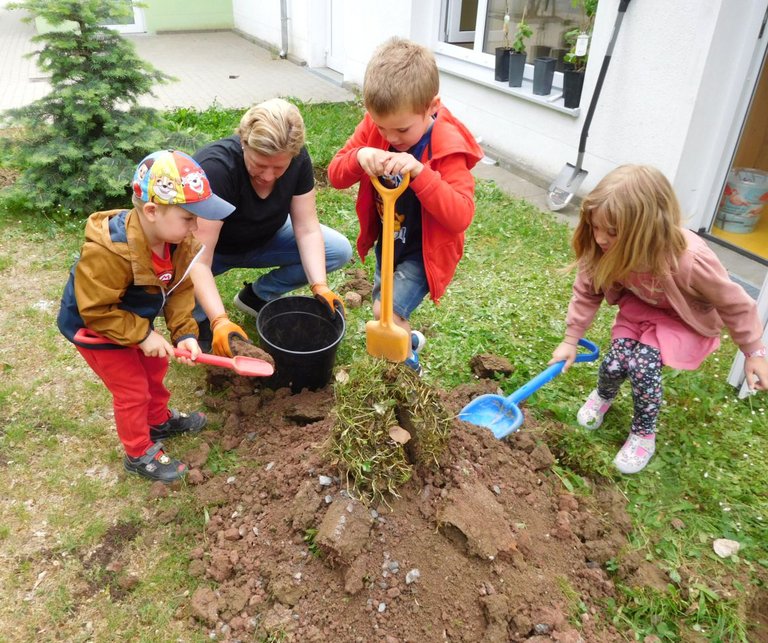 Kinder und eine Erzieherin graben im Garten 